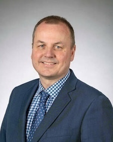 Man in a gray quarter-zip pullover with the Notre Dame logo, looking at the camera.